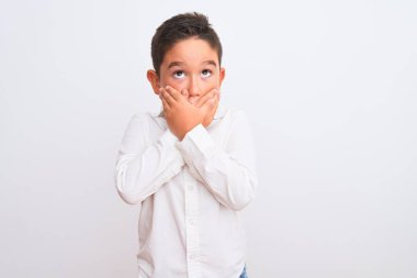 Zarif bir gömlek giyen güzel bir çocuk izole edilmiş beyaz arka planda dikiliyor. Ağzını yanlışlıkla ellerle kapatıyor. Gizli konsept.