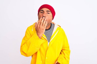 İzole edilmiş beyaz arka planda duran, yağmurluk ve yün şapka giyen orta yaşlı bir adam ağzıyla esnemekten sıkılmış. Huzursuz ve uykulu..