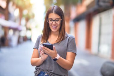 Mutlu ve kendinden emin gülümseyen genç ve güzel bir kadın. Yüzünde gülümsemeyle şehrin caddesinde akıllı telefon kullanarak dikiliyorsun.