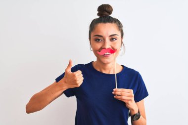 Genç, güzel bir kadın, izole edilmiş beyaz arka planda parti bıyığı tutuyor. Kocaman gülümsüyor ve gülümsüyor. İşaret veriyor.