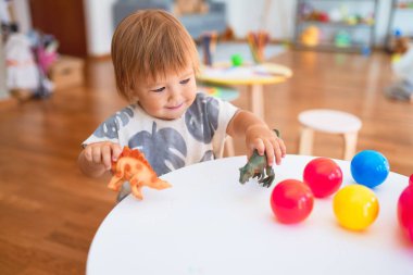Anaokulunda bir sürü oyuncak etrafında dinozorlarla oynayan sevimli bir çocuk.