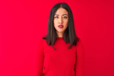 Yüzünde ciddi bir ifade olan, izole edilmiş kırmızı arka planda duran, sıradan giysili, genç, güzel Çinli bir kadın. Basit ve doğal bir şekilde kameraya bakıyorsun..