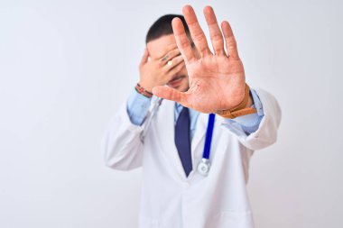 Steteskop takan genç bir doktor, izole edilmiş arka planda ellerle gözleri kapatıyor ve üzgün ve korku ifadeleriyle jestleri durduruyor. Utanç verici ve olumsuz bir kavram..