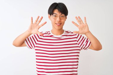 Gözlüklü ve çizgili tişörtlü genç Çinli adam izole edilmiş beyaz arka plan üzerinde duruyor ve parmaklarını on numarayı gösterirken kendinden emin ve mutlu bir şekilde gülümsüyor..