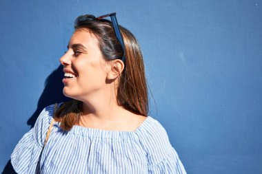 Mavi duvara yaslanan güzel bir kız, güneşli bir yaz gününde gülümseyen genç bir arkadaş.