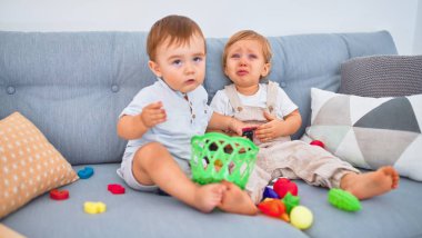 Güzel bebekler, biri ağlıyor, kanepede oturuyor, evde oyuncaklarla oynuyor.