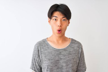 İzole edilmiş beyaz arka plan üzerinde duran sıradan bir tişört giyen genç Çinli bir adam şaşkınlık dolu bir yüz ifadesinden korkuyor ve heyecanlanıyor.