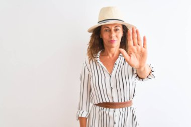 Orta yaşlı iş kadını, çizgili elbise ve izole edilmiş beyaz arka plan üzerine şapka giyip avuç içiyle şarkı söylemeyi kesiyor. Yüzünde olumsuz ve ciddi bir jest olan uyarı ifadesi.