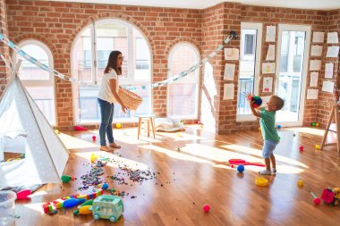 Anaokulunda basketbol oynayan genç ve güzel öğretmen ve bebek hasır sepet ve top oynuyorlar.