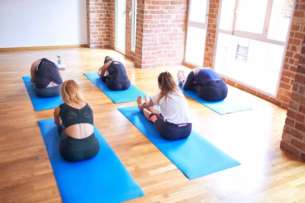 Young beautiful group of sportswomen practicing yoga. Coach teaching seated forward fold to sporty women at gym