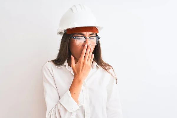 年轻美丽的建筑师女人 戴着头盔和眼镜 戴在孤立的白色背景上 厌烦地打呵欠 双手捂住疲惫的嘴 烦躁不安和困倦 — 图库照片