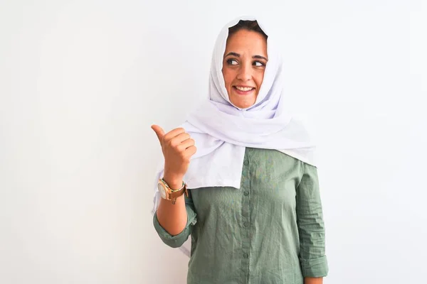 若いです美しいですアラブ女性身に着けています伝統的なイスラム教徒のヒジャーブ上の隔離された背景笑顔で幸せな顔を見て 親指アップで側面を指して — ストック写真