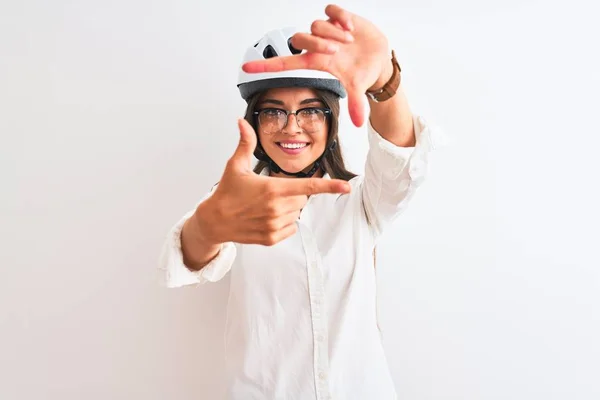 Beautiful businesswoman wearing glasses and bike helmet over isolated white background smiling making frame with hands and fingers with happy face. Creativity and photography concept.