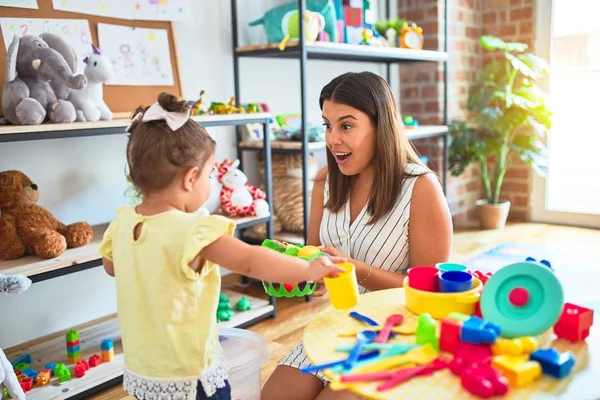 Young beautiful teacher and toddler playing with dishes, cutlery and cups toy on the table at kindergarten — Stock Image Young Beautiful Teacher Toddler Playing Dishes Cutlery Cups Toy Table Stock Photo