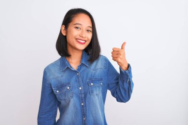 İzole edilmiş beyaz arka planda duran kot gömlek giyen genç, güzel Çinli bir kadın mutlu bir el hareketi yapıyor. Kameraya bakıp başarıyı gösteren ifade onaylanıyor.