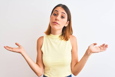 Sarı yaz tişörtü giyen güzel kızıl saçlı kadın izole edilmiş arka plan hakkında hiçbir şey bilmiyor ve elleri ve kolları havada şaşkın bir ifade sergiliyor. Şüphe kavramı.