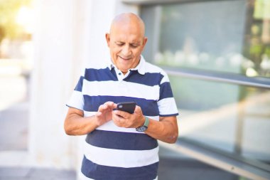 Kıdemli yakışıklı adam mutlu ve kendinden emin gülümsüyor. Yüzünde gülümsemeyle şehrin caddesinde akıllı telefon kullanarak dikiliyorsun.