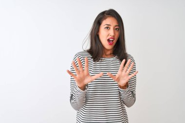 İzole edilmiş beyaz arka plan üzerinde duran çizgili tişört giyen genç, güzel Çinli kadın korku ifadesinden korkuyor ve dehşete düşüyor. El hareketlerini durdur, şok içinde bağır. Panik konsepti.