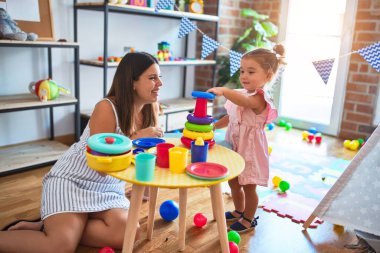 Genç, güzel öğretmen ve bebek, anaokulundaki masada halkalar kullanarak piramit inşa ediyorlar.