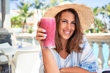 Güzel bir kadın oteldeki barın havuzunda oturmuş yaz tatili için sağlıklı meyve suyu içiyor.