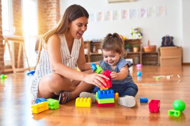 Young beautiful teacher and toddler playing with building blocks toy at kindergarten clipart