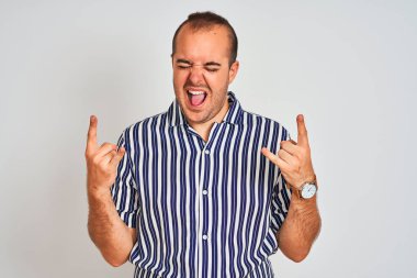 Mavi çizgili gömlekli genç adam izole edilmiş beyaz arka planda duruyor çılgın bir ifadeyle el kaldırarak rock sembolü yapıyor. Müzik yıldızı. Ağır konsept.