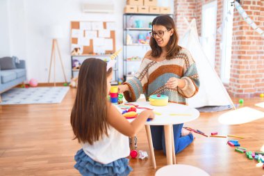 Güzel öğretmen ve çocuk gülümsüyor. Anaokulundaki oyuncakların etrafında plastik yemek ve çatal bıçak kullanarak yemek oynuyorlar.