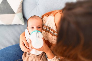 Genç, güzel bir kadın ve bebeği evdeki kanepede. Yeni doğan ve anne rahatlıyor ve dinleniyor. Beslenme şişesini kullanarak süt içiyorlar.