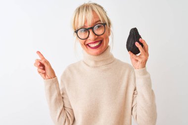 İzole edilmiş beyaz arka planda avakado tutan orta yaşlı kadın elini ve parmağını kenarı işaret ederek çok mutlu.