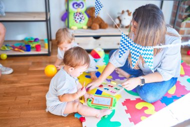 Beautiful teacher and toddlers playing around lots of toys at kindergarten clipart