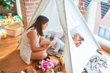 Anaokulunda Tip 'in içinde yerde yatan sarışın kıza güzel bir öğretmen kitabı okuyor.