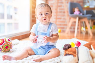 Anaokulunda battaniyenin üzerinde bir sürü oyuncağın etrafında oturan güzel çocuk.