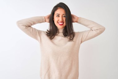 Balıkçı yaka kazak giyen güzel Çinli kadın izole edilmiş beyaz arka planda duruyor. Kolları ve elleri başının arkasında, mutlu bir şekilde gülümsüyor.