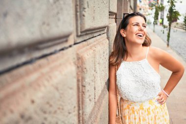 Güzel kız duvara yaslanıyor, genç arkadaş canlısı kadın mutlu bir yaz gününde gülümsüyor.