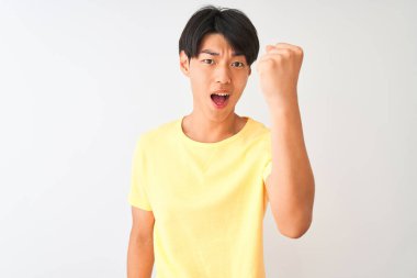 Sarı günlük tişört giyen Çinli bir adam izole edilmiş beyaz arka planda kızgın ve kızgın duruyor öfkeyle bağırırken yumruğunu kaldırıyor. Öfke ve agresif kavram.