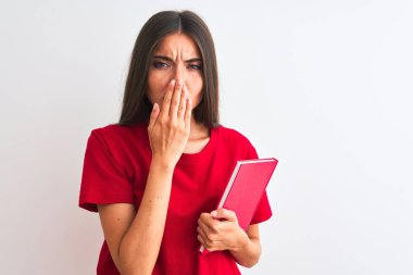 Genç, güzel bir kız öğrenci elinde kırmızı bir kitapla izole edilmiş beyaz arka planda duruyor. Ağzı kapalı, utancından ağzı açık, korkusunun dışa vurumu, sessizlikten korkması, gizli konsept.