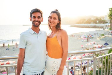 Tatilde mutlu ve kendinden emin gülümseyen genç bir çift. Yüzünde gülümsemeyle sahilde sarılırken