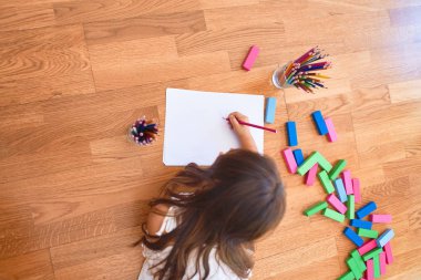 Adorable toddler lying down on the floor drawing using paper and pencils at kindergarten clipart