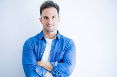 Denim gömlek giyen genç yakışıklı adam izole beyaz arka plan üzerinde duran mutlu yüz kameraya bakarak çapraz kolları ile gülümseyerek. Pozitif kişi.