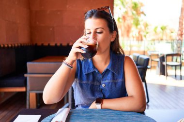 Genç ve güzel bir kadın restoranda oturmuş yaz tatilinin tadını çıkarıyor taze soda içiyor.