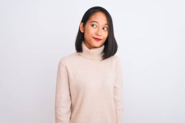 Balıkçı yaka kazak giyen genç Çinli bir kadın izole edilmiş beyaz arka planda durup gülümsüyor ve başka tarafa bakıyor..