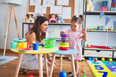 Genç, güzel öğretmen ve bebek, anaokulundaki masada halkalar kullanarak piramit inşa ediyorlar.