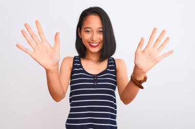 İzole edilmiş beyaz arka plan üzerinde duran çizgili tişört giyen genç Çinli kadın on numarayı gösterirken kendinden emin ve mutlu bir şekilde gülümsüyor..