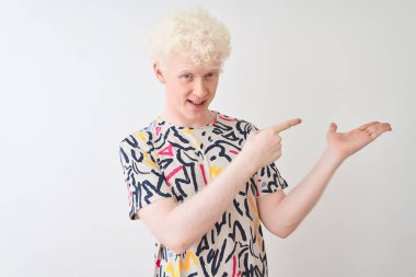 Renkli tişört giyen genç albino adam izole edilmiş beyaz arka planda durup hayrete düşmüş ve kameraya gülümserken eliyle parmakla işaret ediyor..