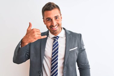 Takım elbiseli ve kravatlı genç yakışıklı iş adamı izole edilmiş arka planda gülümsüyor telefonla el ve parmak hareketleri yapıyor telefonda konuşuyor gibi. İletişim kavramları.