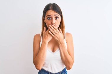 Güzel kızıl saçlı kadın, izole edilmiş arka planda günlük beyaz tişört giyiyordu. Ağzını yanlışlıkla ellerle kapatıyordu. Gizli konsept.