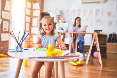 Beyaz kız çocuk, bayan öğretmenle oyun oynayıp öğreniyor. Anne ve kızı oyun odasında oyuncakların etrafında manyetik karatahtaya resim çiziyorlar.