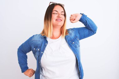 Güzel bir kadın kot gömlek giyiyor, izole edilmiş beyaz arka plan üzerinde duruyor, yorgun ve rahat, uykulu ve sabahın erken saatlerinde esniyor.