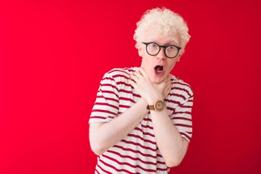 Genç albino sarışın adam çizgili tişört ve gözlüklerle izole edilmiş kırmızı arka planda bağırıyor ve boğuluyor çünkü acı verici bir boğulma var. Sağlık problemi. Boğulma ve intihar konsepti.
