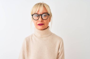 Balıkçı yaka kazak ve gözlük takan orta yaşlı bir kadın izole edilmiş beyaz bir arka plan ve yüzünde ciddi bir ifade var. Basit ve doğal bir şekilde kameraya bakıyorsun..